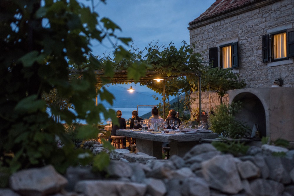 A long table set for a wine tasting under vines in a countryside courtyard
