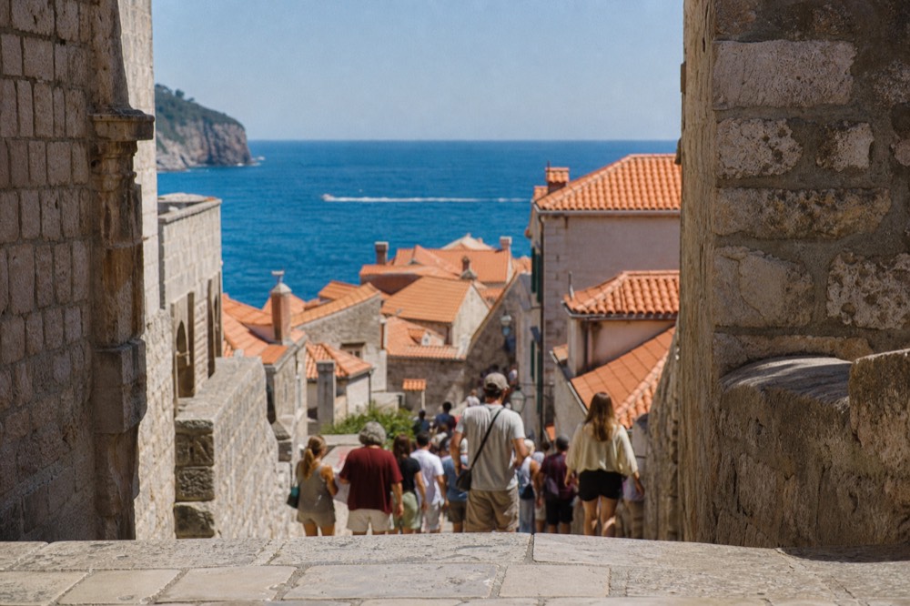 Crowded limestone street with streams of visitors walking between stone buildings