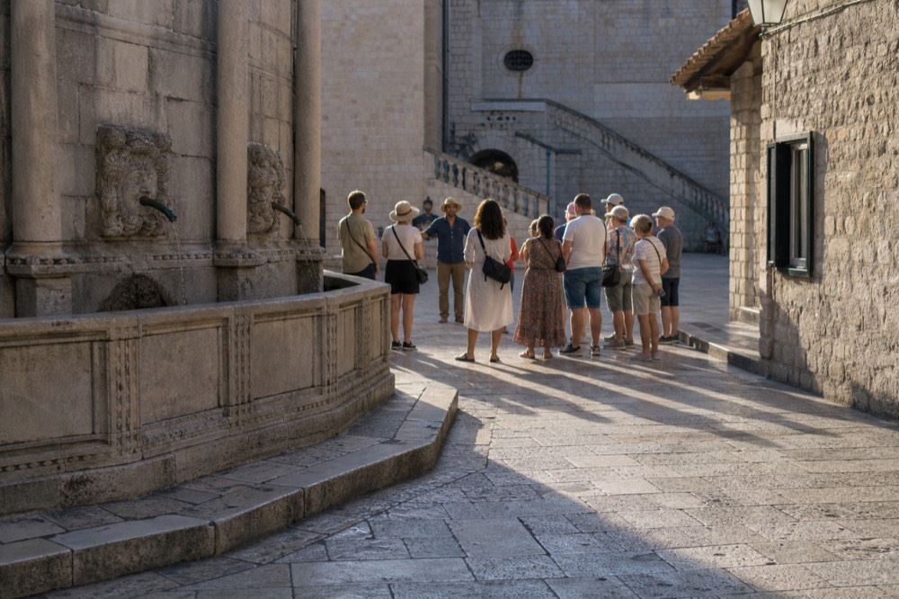 Tour guide speaking to a small group beside a stone fountain in an old town square