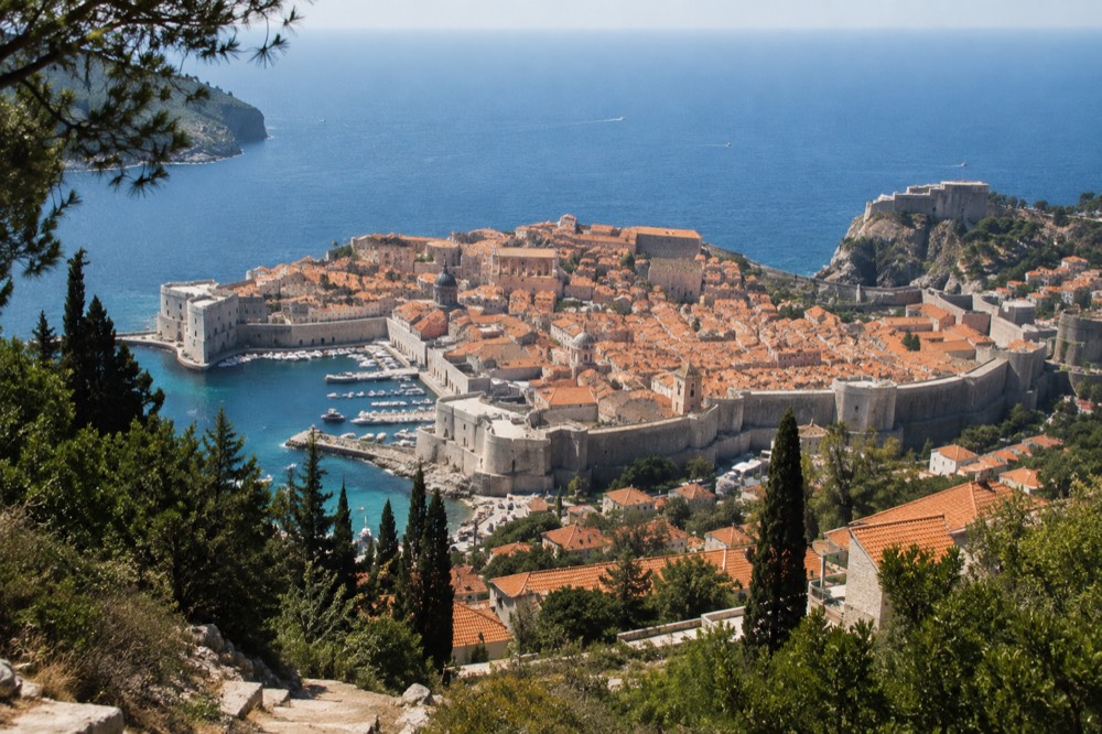 A walled old town with terracotta roofs beside a blue sea at midday