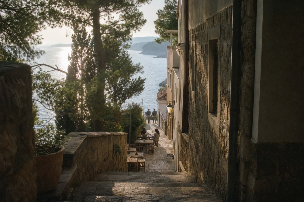 A narrow stone street in an old town with small tables set outside a wine bar