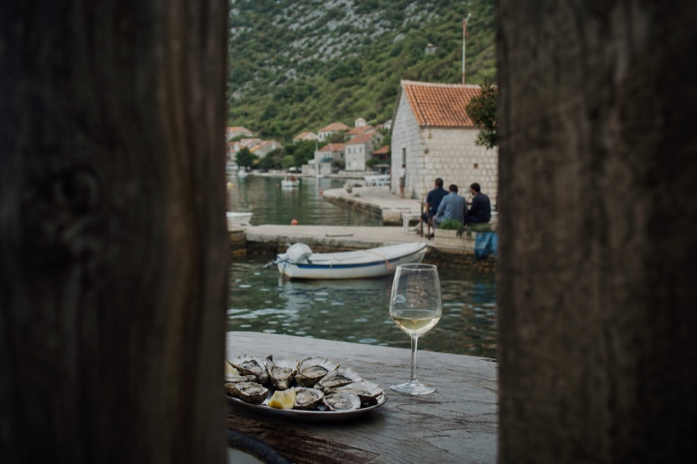 Fresh oysters on a tray beside a glass of white wine at a waterside table