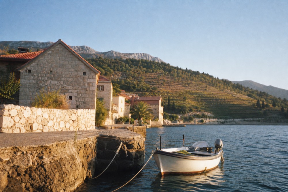 A small boat moored beside a stone quay with hills and vineyards behind