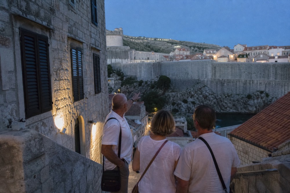 A guide gesturing toward the fortified walls of Dubrovnik while speaking to a couple