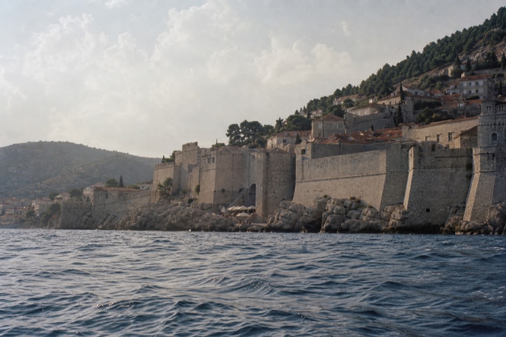 The stone city walls of Dubrovnik curving above red rooftops toward the sea