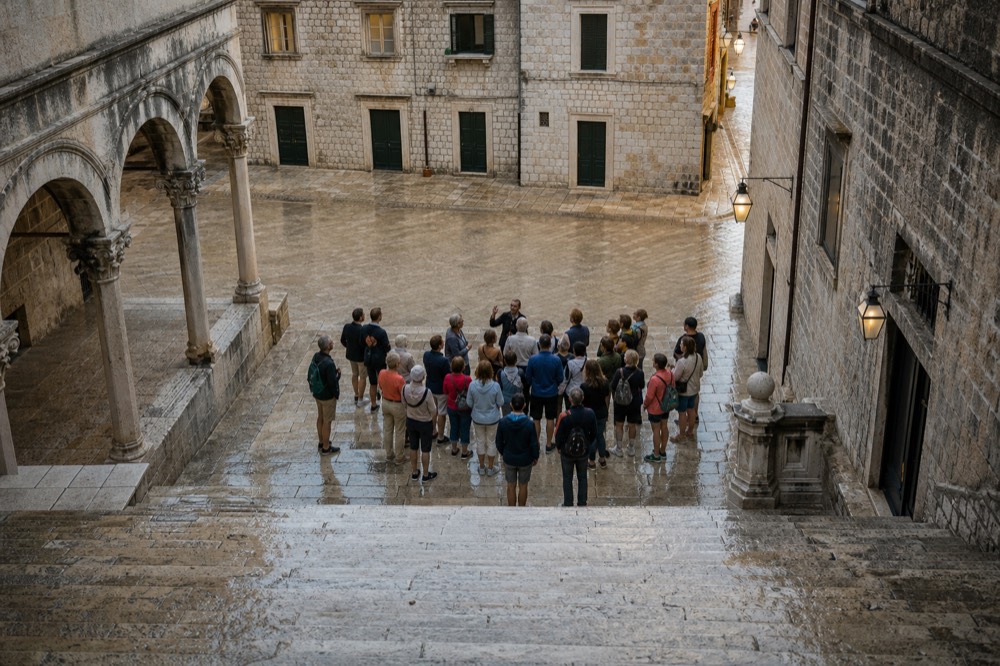A small group of walkers gathered around a guide at dusk in a Dubrovnik square