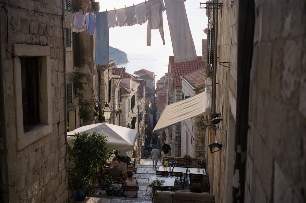 Narrow stone lane in Dubrovnik Old Town with laundry above and café tables below