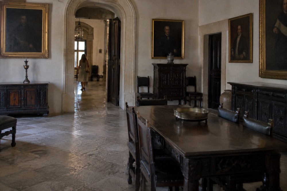 Interior hall with dark wooden furniture, portraits on walls and a stone floor