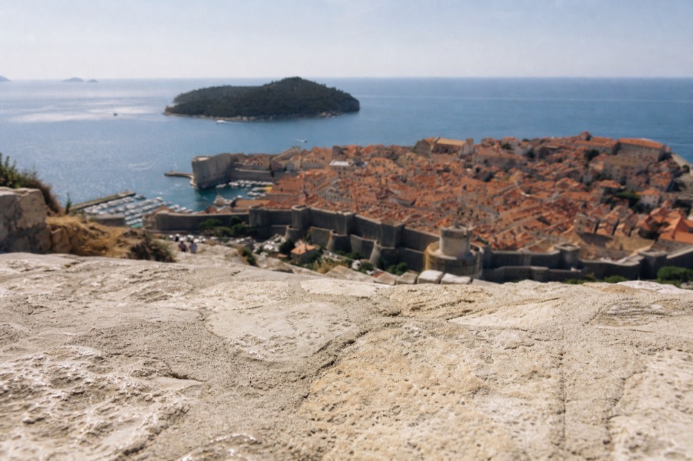 Wide view of the walled city from a hillside above, with the sea and an island in the distance