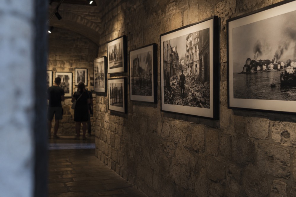 A dimly lit gallery wall covered with framed black and white wartime photographs