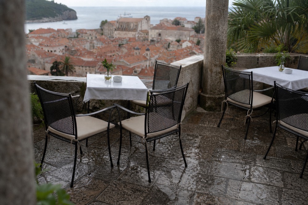 Stone terrace restaurant tables set above Dubrovnik rooftops with the sea beyond
