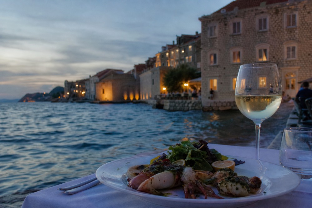 Elegant plated seafood dish on a white tablecloth beside a wine glass