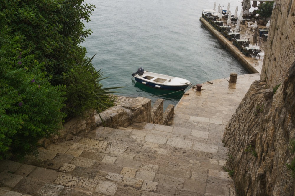 Small boat moored beside a stone quay with restaurant tables in the background