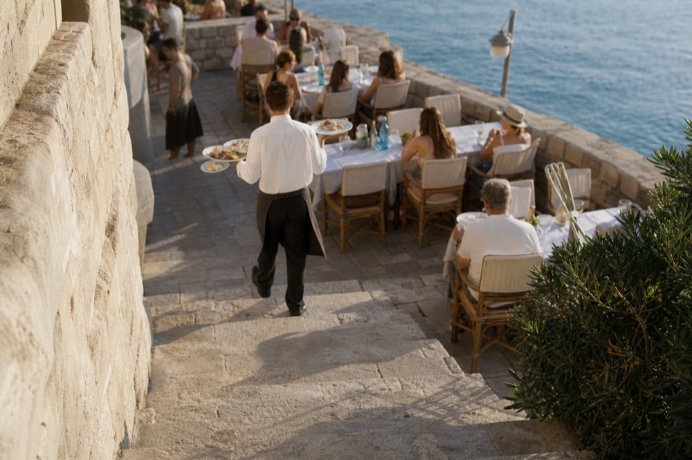 A waiter carrying plates between closely set tables on an evening terrace
