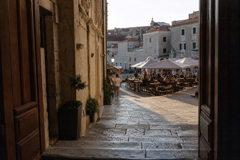 Diners at outdoor tables on a stone square in warm evening light