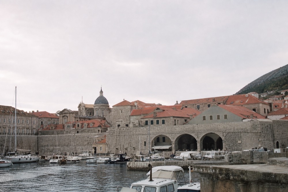 A harbour lined with masts and small boats below old stone walls