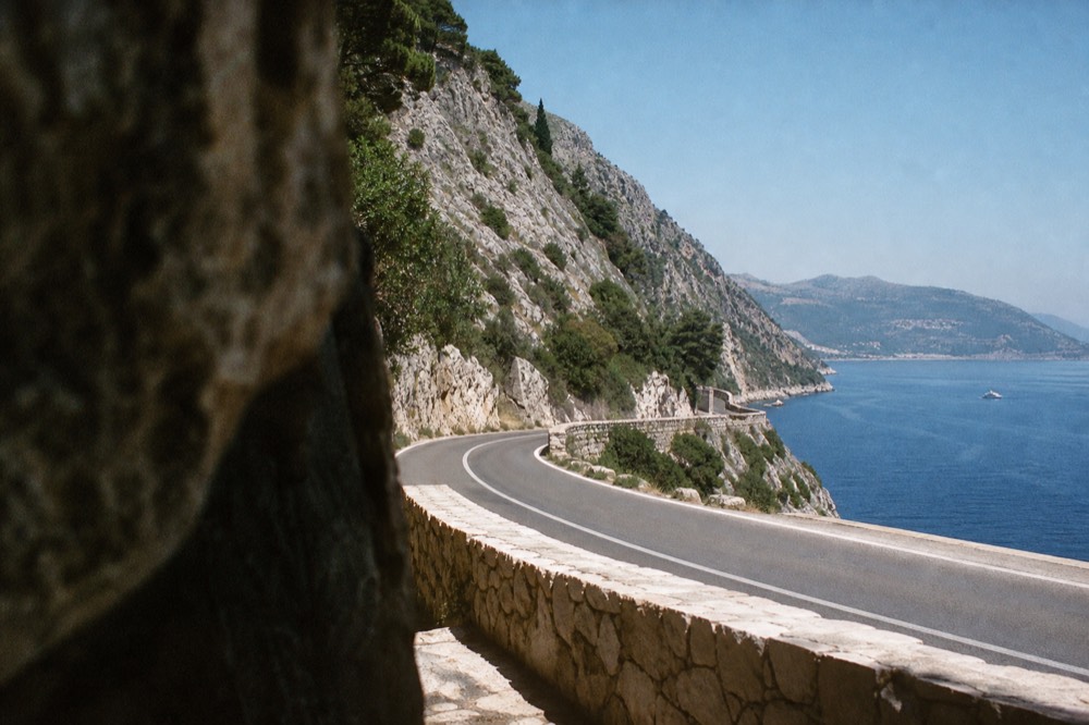 A winding coastal road with steep mountains above a blue bay