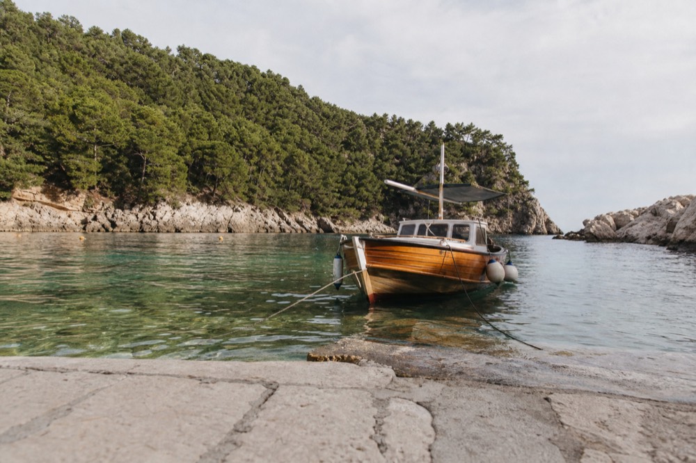 A wooden boat anchored in a clear green bay surrounded by pine trees