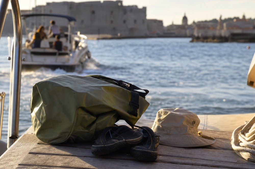 A dry bag, sun hat and water shoes arranged on a wooden boat deck