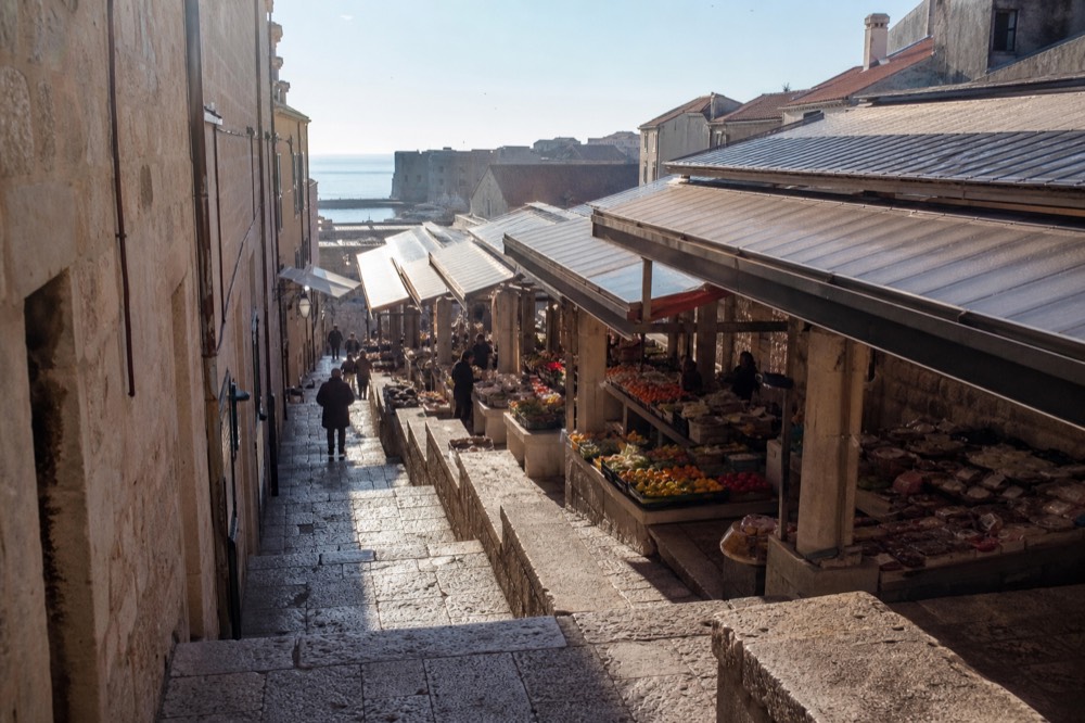 A covered market hall with stalls of vegetables, cheese and household goods
