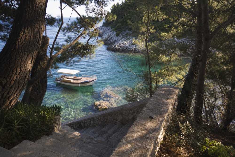 A wooden boat moored in clear green water beside a rocky island shore