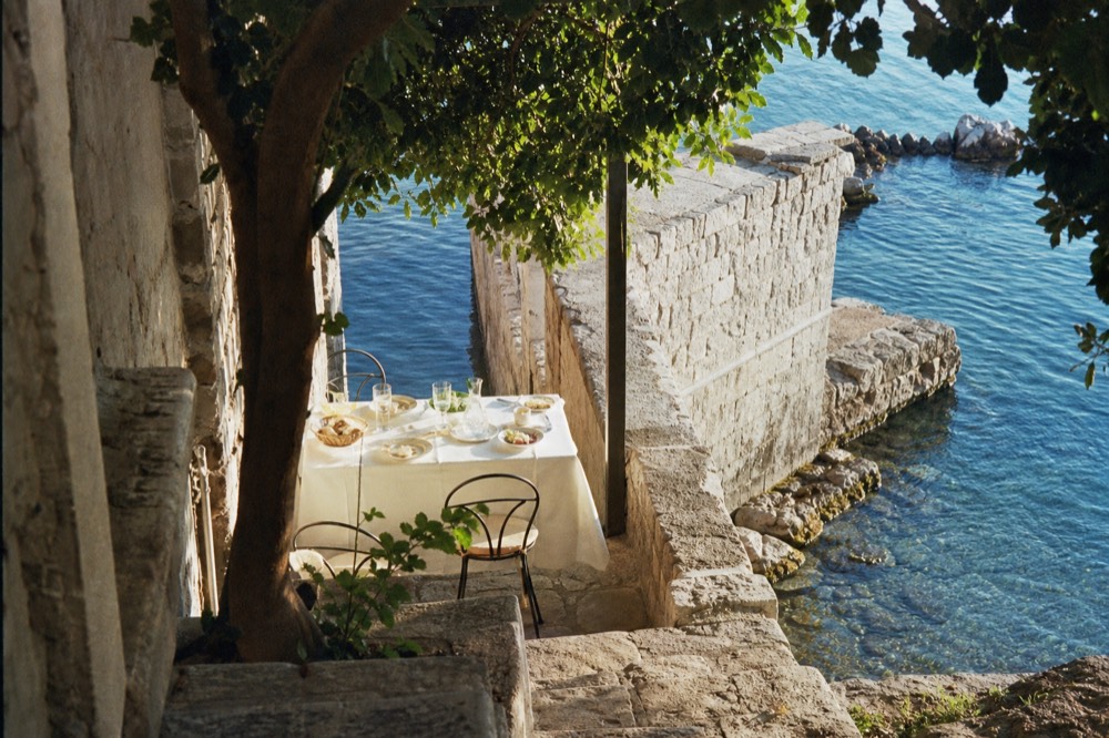 A vine-shaded terrace table set for lunch beside a stone harbour wall