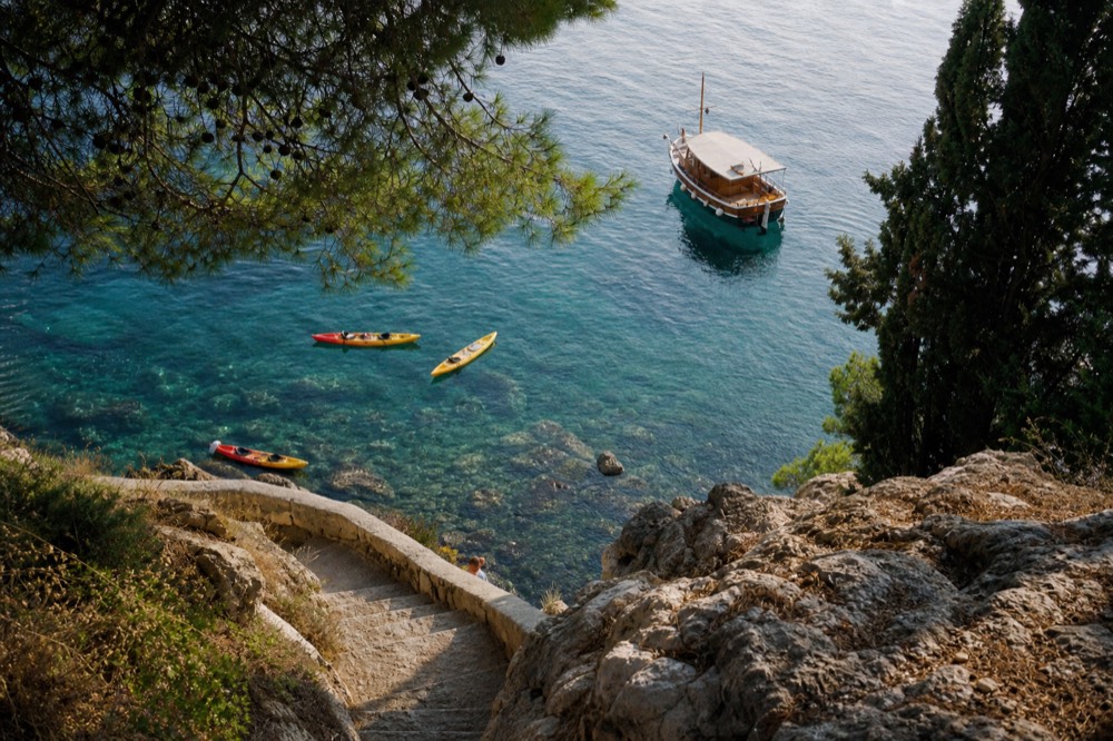 Kayaks floating in clear water beside a wooden boat near Dubrovnik