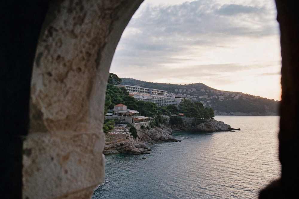 Tree-lined bay with hotel terraces above a rocky shoreline at dusk