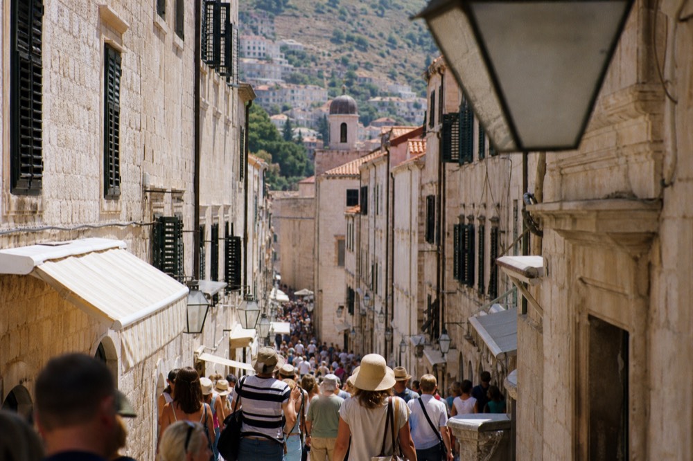 Crowded marble street with stone buildings on both sides under midday sun