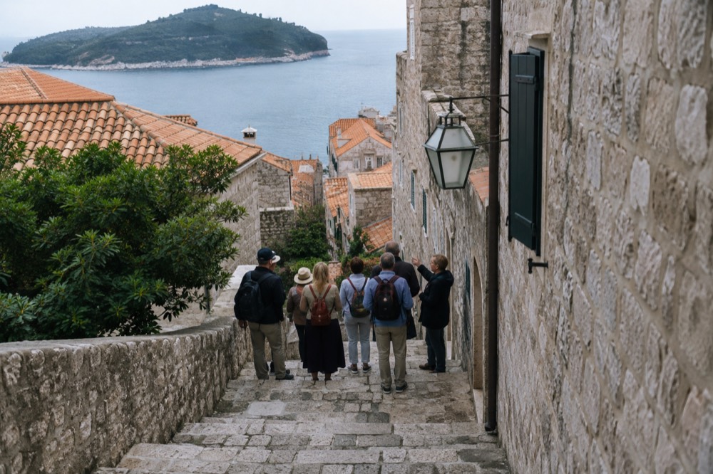 Tour guide speaking to a small group beside old stone buildings in a narrow lane