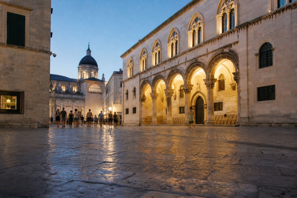 Lit stone square at dusk with a palace facade glowing under lamps