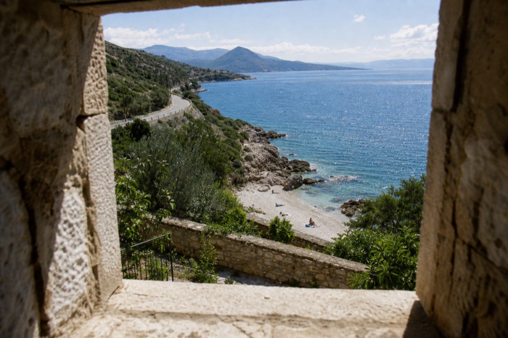 A coastal road curving along a peninsula with vineyards sloping to the sea