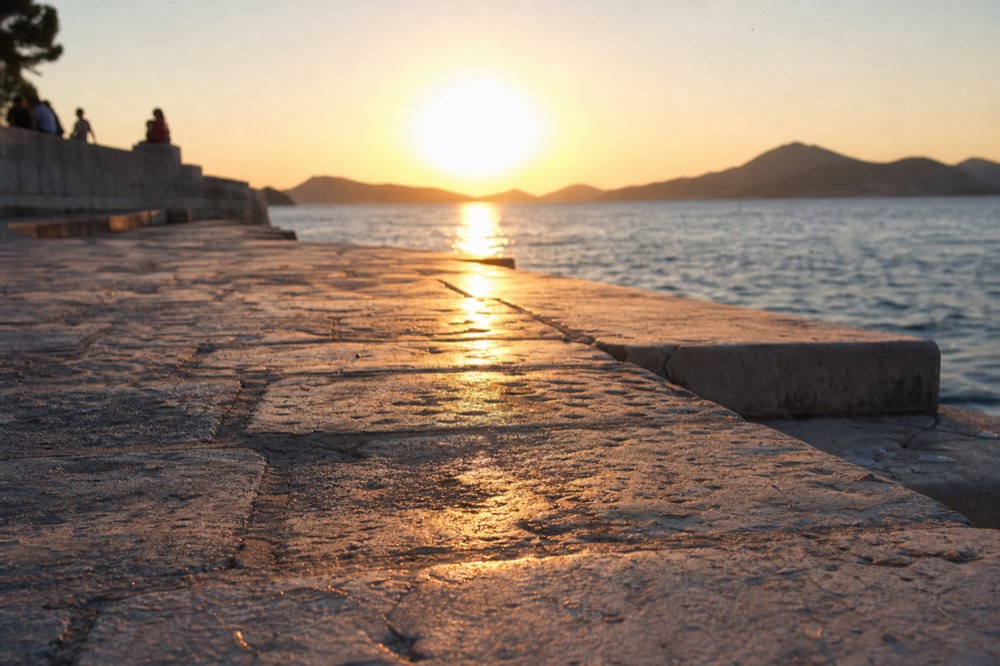 A sunset over the sea with silhouetted islands on the horizon seen from a stone quay