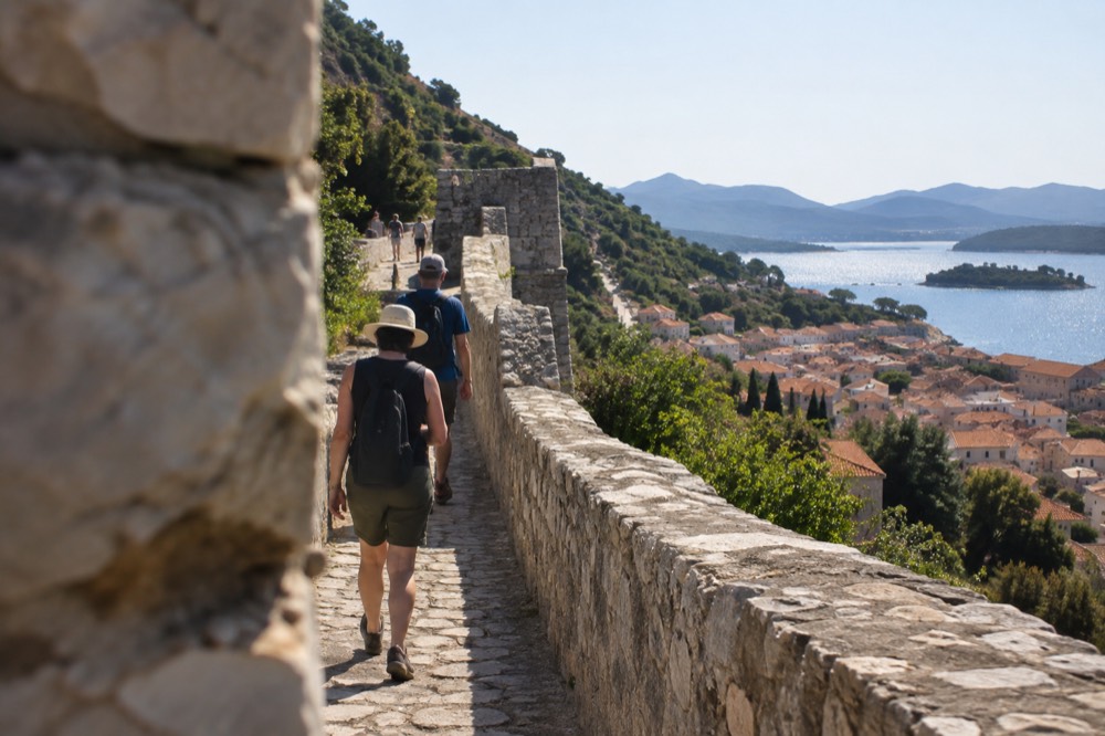 Walkers on a stone wall path high above a coastal town and islands