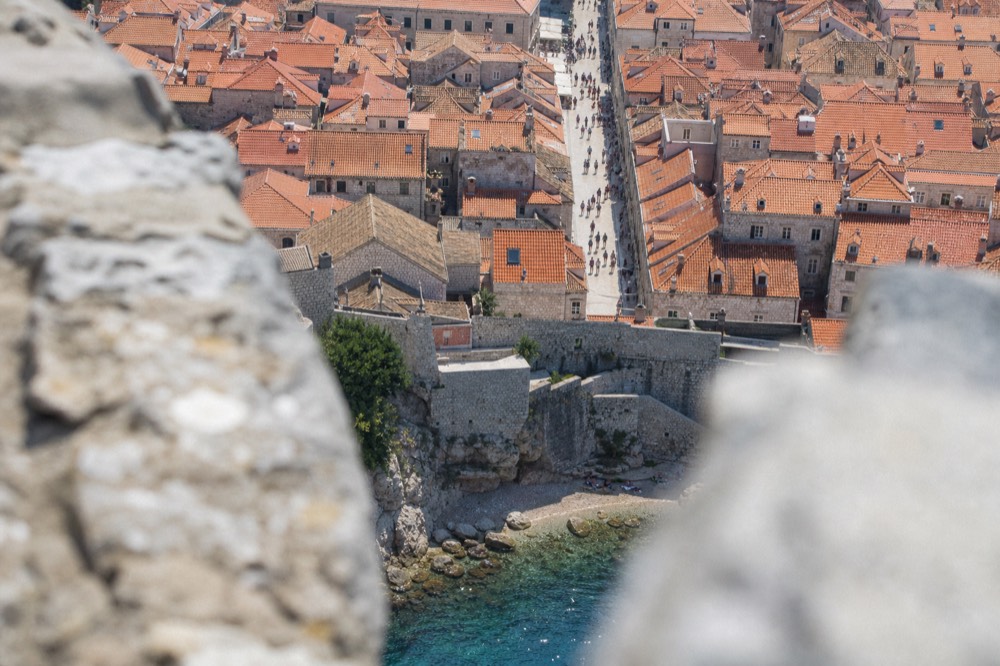 Walled city rooftops seen from a high vantage point with a pale street running through the middle