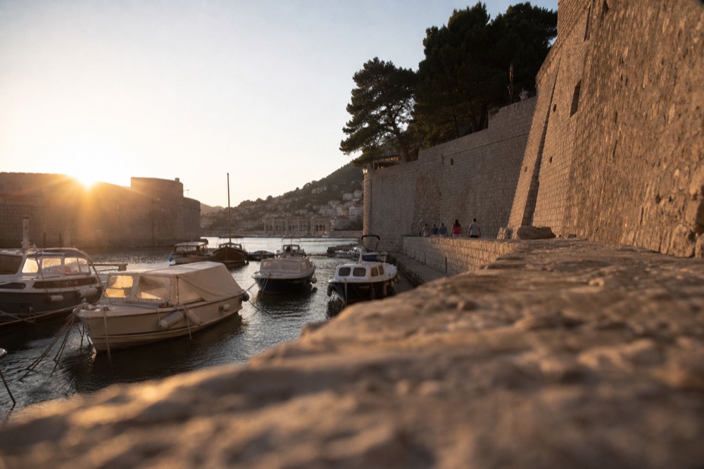 Old city port with small boats moored beside stone walls at golden hour