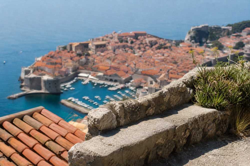 The walled city of Dubrovnik seen from a hillside above red rooftops and the sea