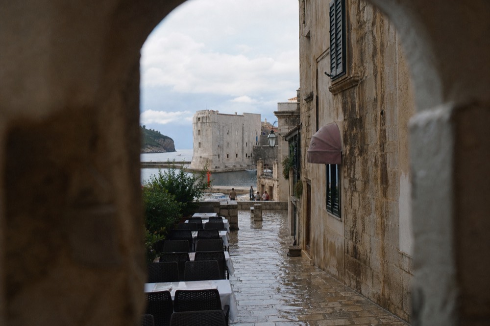 A restaurant terrace with white tablecloths on stone paving beside old Dubrovnik buildings