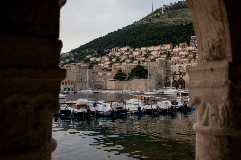 A harbour with moored boats and a hillside town behind them in evening light
