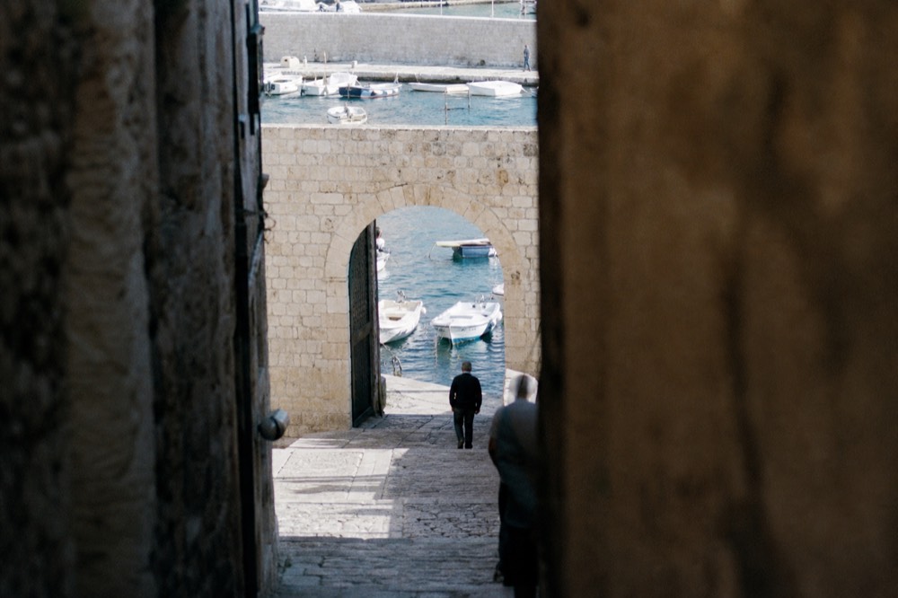 A stone gate opening onto a harbour with small boats moored in clear water