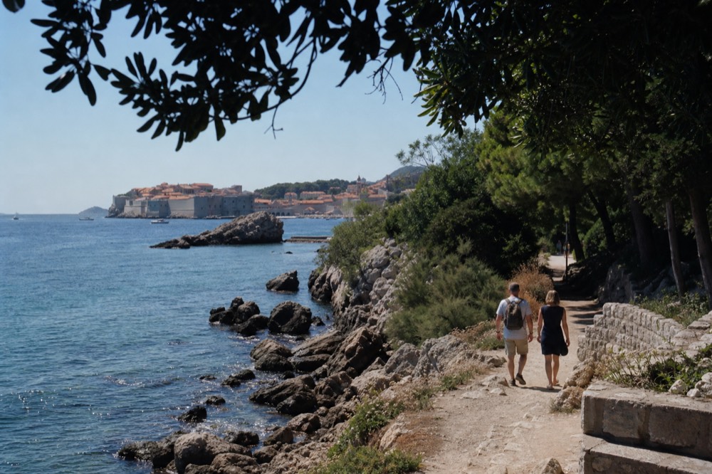 A coastal path beside the sea with trees and a distant walled town