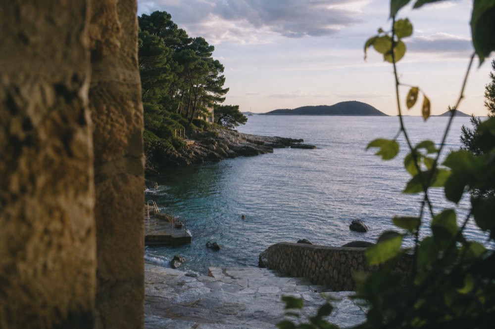 A calm swimming bay with clear water and low evening light over distant islands