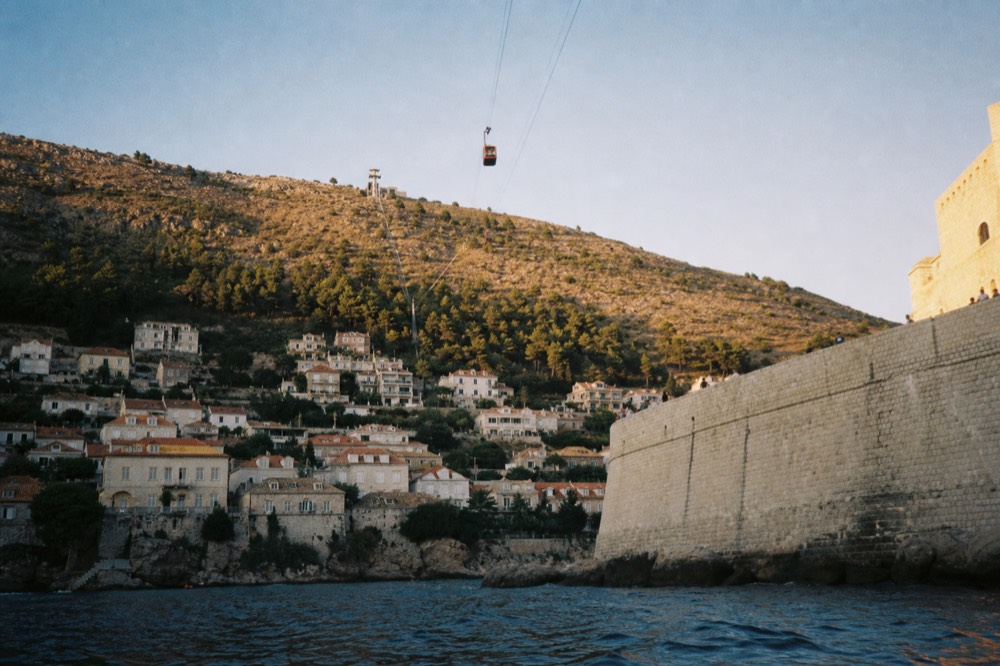 A cable car cabin travelling up a steep hillside above a coastal city in evening light