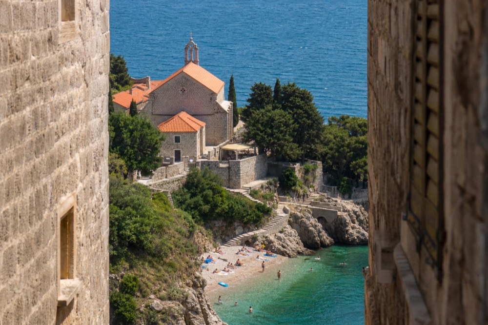 A stone church and terrace above a small pebble beach with wooded cliffs on either side