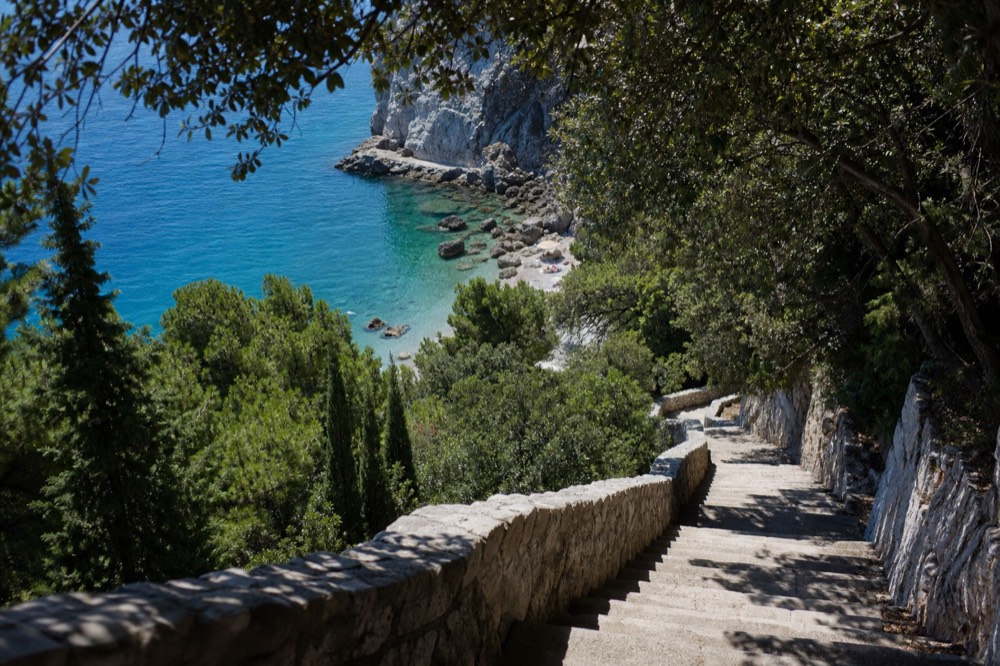 A long stone staircase descending through trees toward a small beach cove