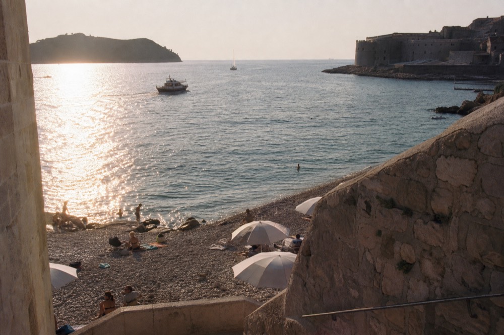 Pebble beach with clear shallow water and sun umbrellas along the Dubrovnik coastline