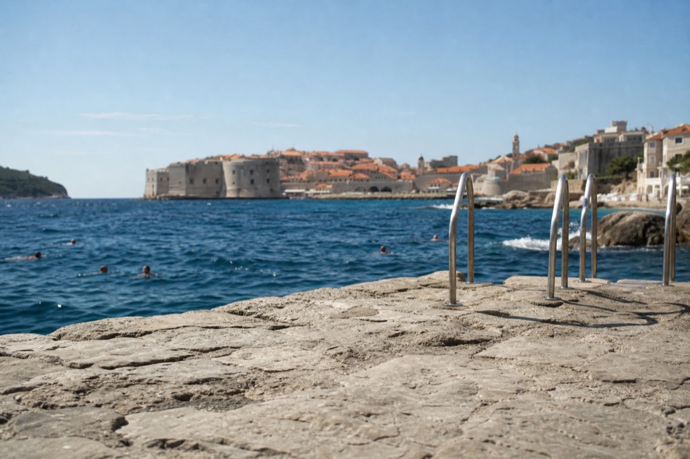 Rocky swimming platform with swimmers in deep blue water on the Dubrovnik coast