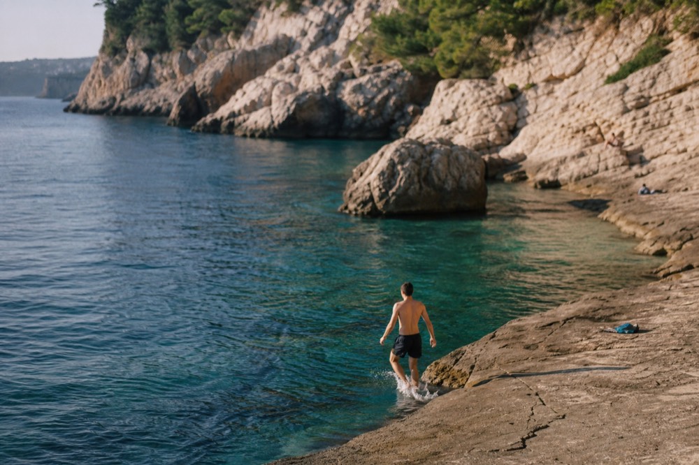 Swimmer entering clear water from a flat rock ledge with limestone cliffs behind