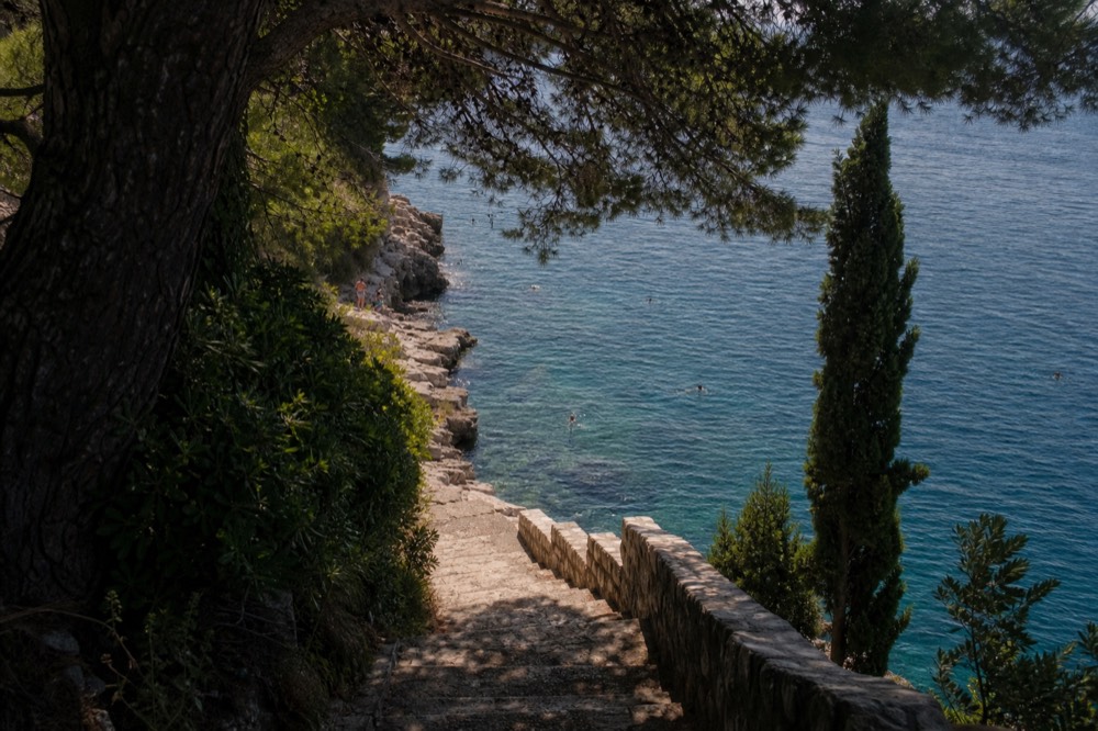 Swimmers in deep clear blue water beside a rocky shoreline