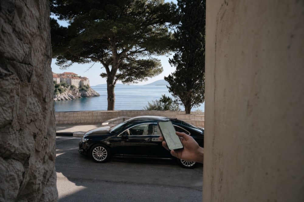 A smartphone showing a ride-hailing app map over a Dubrovnik street scene